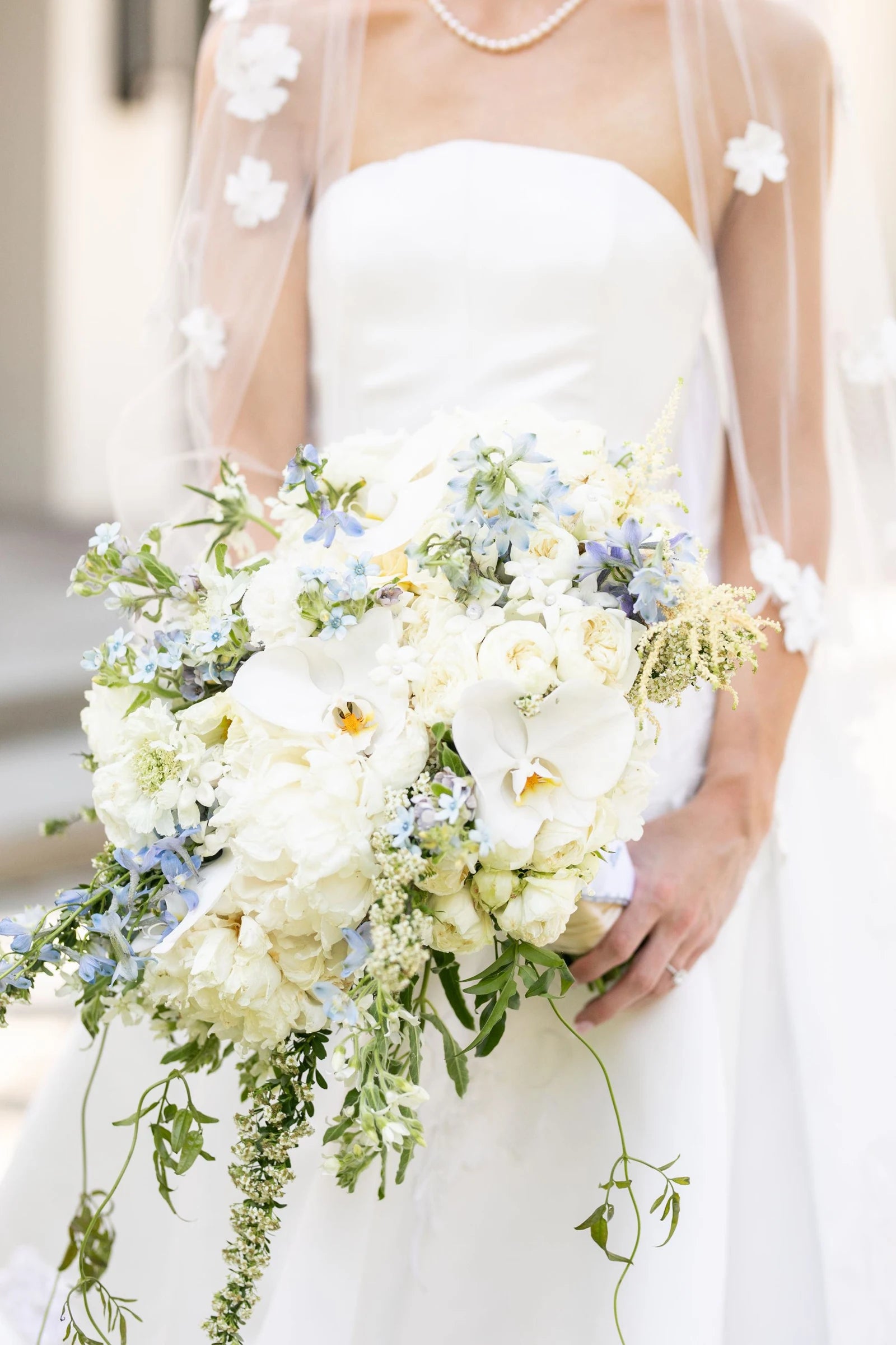 A bride carrying a bouquet of white orchids and pale blue flowers