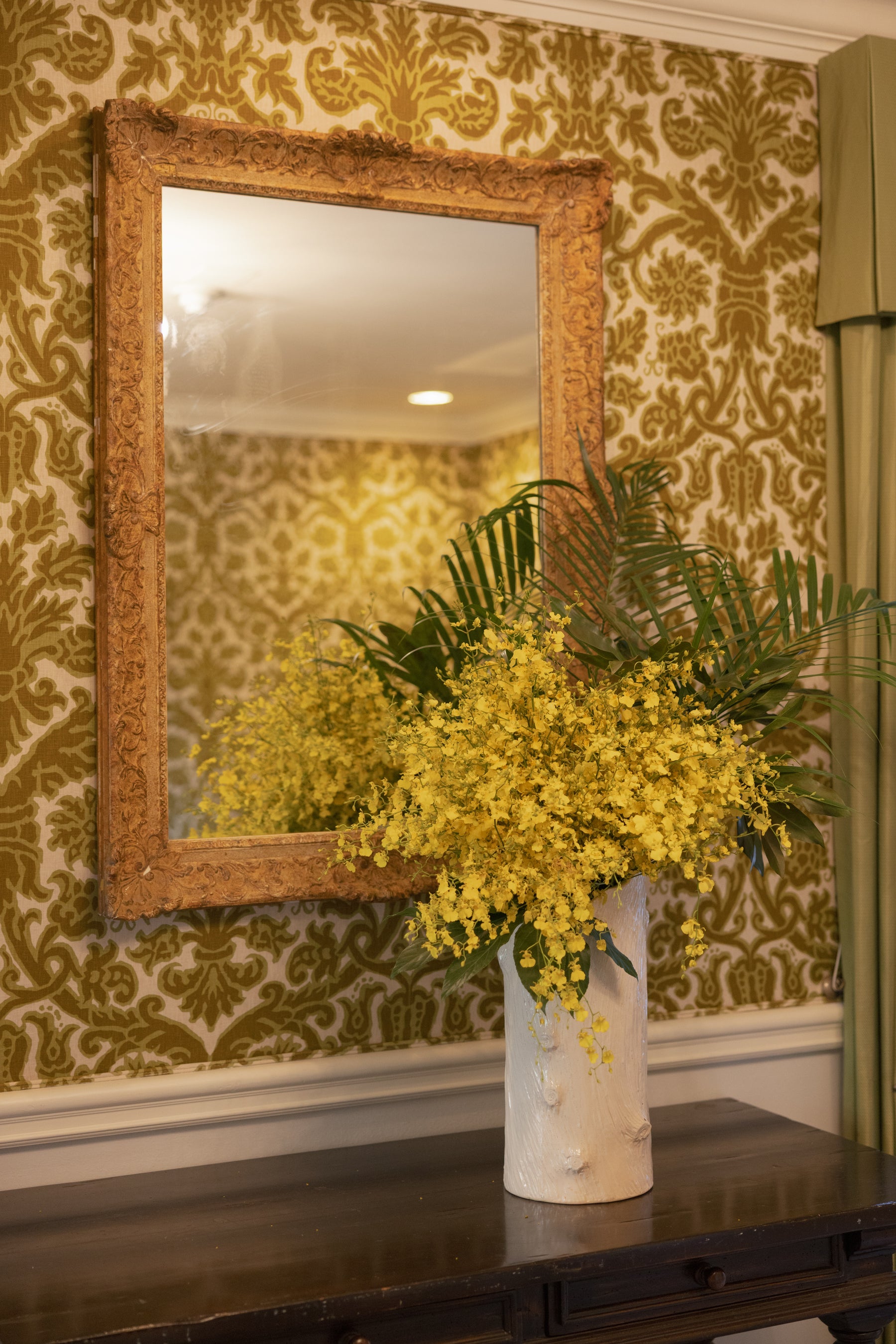 Yellow flowering branches beside an ornate gold mirror