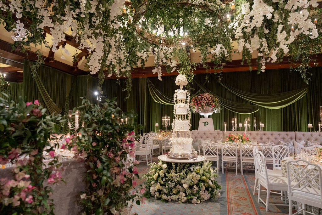 Wedding reception with suspended white flowers, greenery, and a floral cake display
